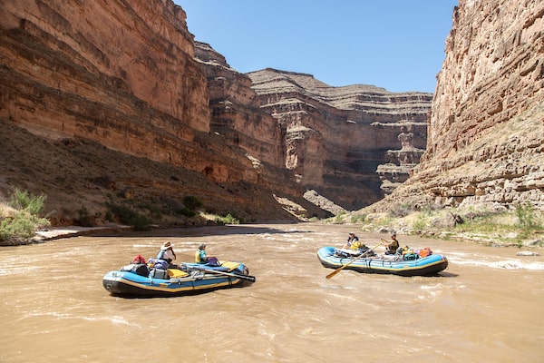 Two rafts flow down a river through a canyon