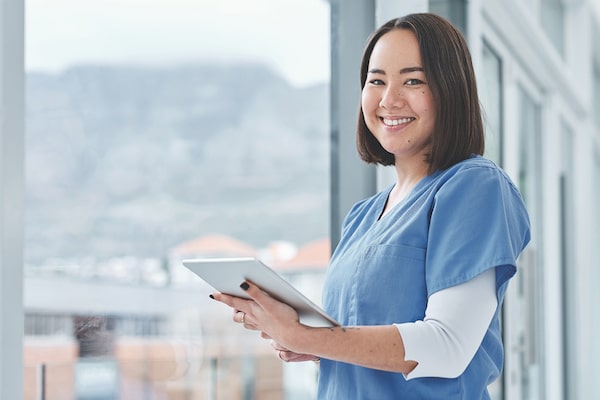 A nurse stands in scrubs holding charts.