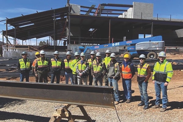 A construction team stands in front of the Schlessman Family Hall construction site.