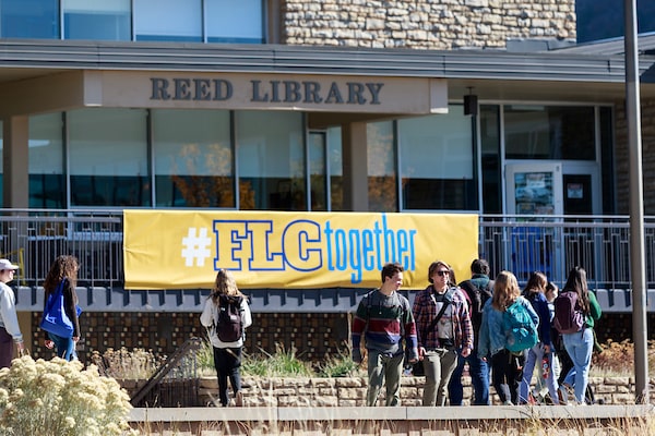 People walk across campus in front of the library sign that reads, FLC Together