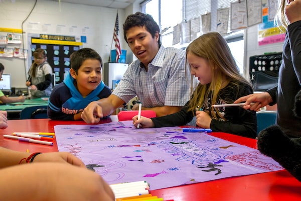 A teacher education student works with elementary school kids on a poster.